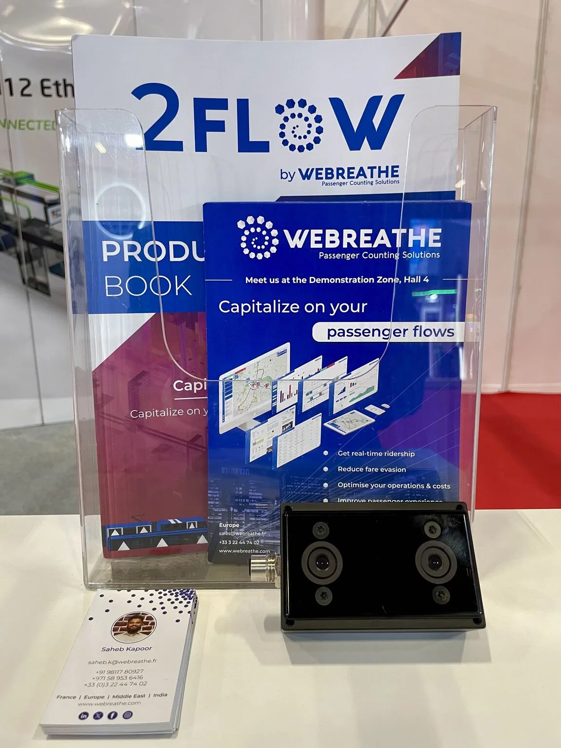 WEBREATHE booth display with 2FLOW brochures, business cards, and a passenger-counting sensor